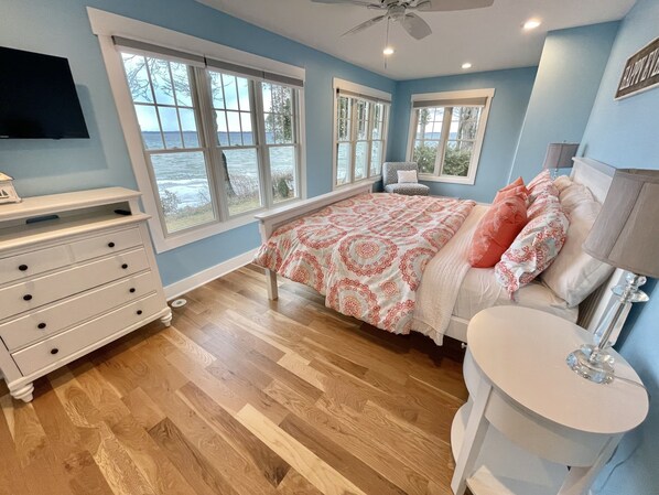 A bedroom with a bed, dresser, vanity, and large windows.
