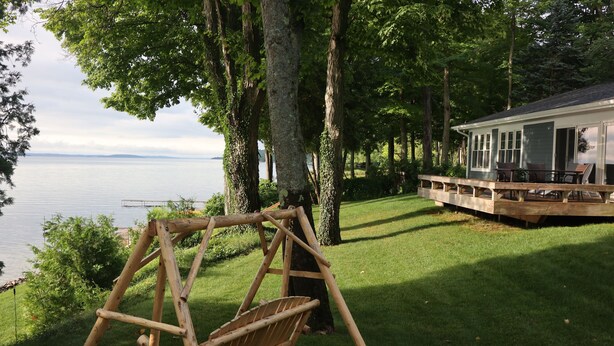 A wooden swing set in a grassy area with a house and dock in the background.