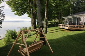 A wooden swing set in a grassy area with a house and dock in the background.