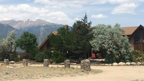 A rustic cabin with a stone foundation, surrounded by a dry, grassy landscape with mountains in the background.