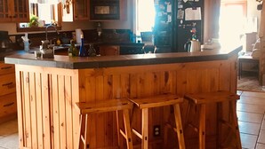 A kitchen with wooden cabinets, a central island with stools, pendant lights, and a refrigerator with magnets.