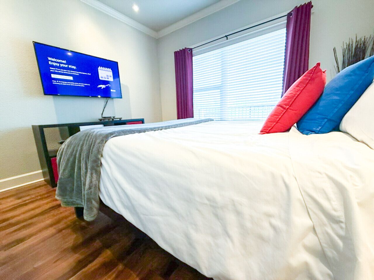 A modern hotel room with a bed, a flat-screen TV mounted on the wall, and a window with curtains.