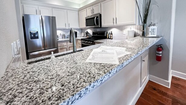 Cozinha moderna com bancadas de granito, eletrodomésticos de aço inoxidável e armários brancos.