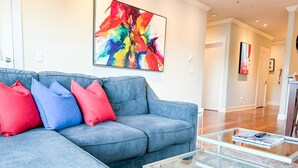 Uma sala de estar moderna com um sofá seccional cinza, almofadas vermelhas e azuis, uma mesa de centro de vidro e arte abstrata na parede.