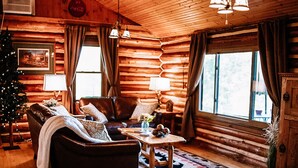A cozy log cabin interior with a leather sofa, armchairs, a coffee table, and a Christmas tree.