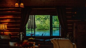 Een gezellig chaletinterieur met een groot raam dat uitkijkt op een rivier en bos.