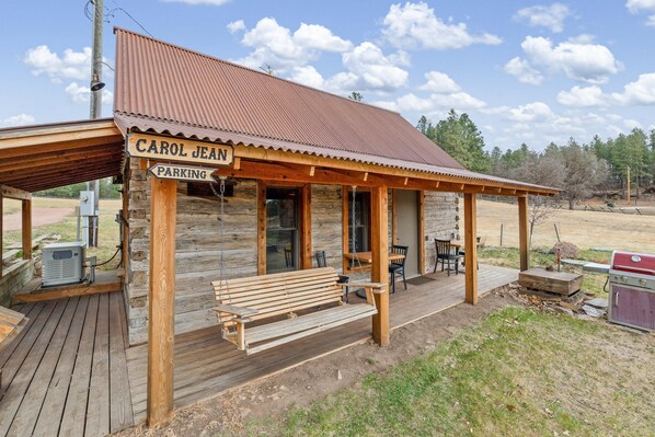 Une cabane en bois avec une véranda, un banc et une pancarte indiquant : « PARCING RÉSERVÉ À CAROL JEAN ».