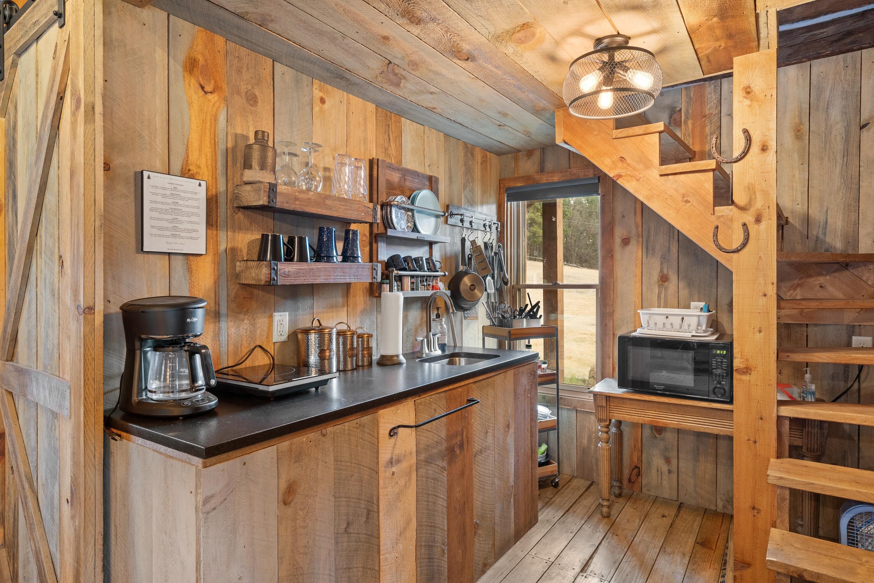 A rustic kitchen with wooden walls, a coffee maker, a microwave, and various kitchen utensils.