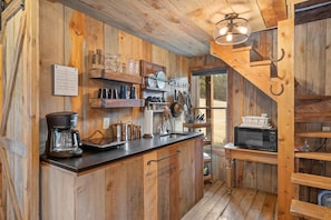 A rustic kitchen with wooden walls, a coffee maker, a microwave, and various kitchen utensils.
