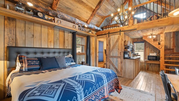 A rustic wooden interior with a bed, a dining table, and a staircase. - Quiet, Comfy Black Hills Cabin; Within 10 Mi of Mt. Rushmore & Custer State Park (Keystone)