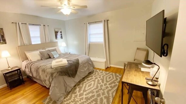 A bedroom with a bed, bedside tables, a desk, a chair, a TV, and a ceiling fan.