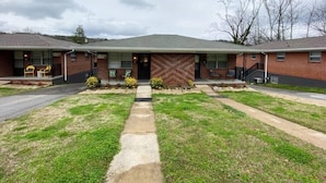 A two-story brick building with a flat roof, a central entrance, and a small porch area with chairs.