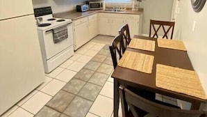 A compact kitchen with white cabinets, a stove, a microwave, and a dining table with chairs.