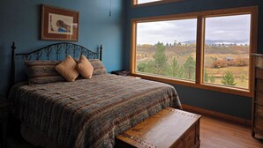 A bedroom with a large window, a bed with patterned bedding, and a picture on the wall. - Book now for hunting and ski seasons. Huge mountain views! (Pagosa Springs)