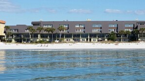 Un hotel frente a la playa con varios pisos, balcones y una playa arenosa al fondo.