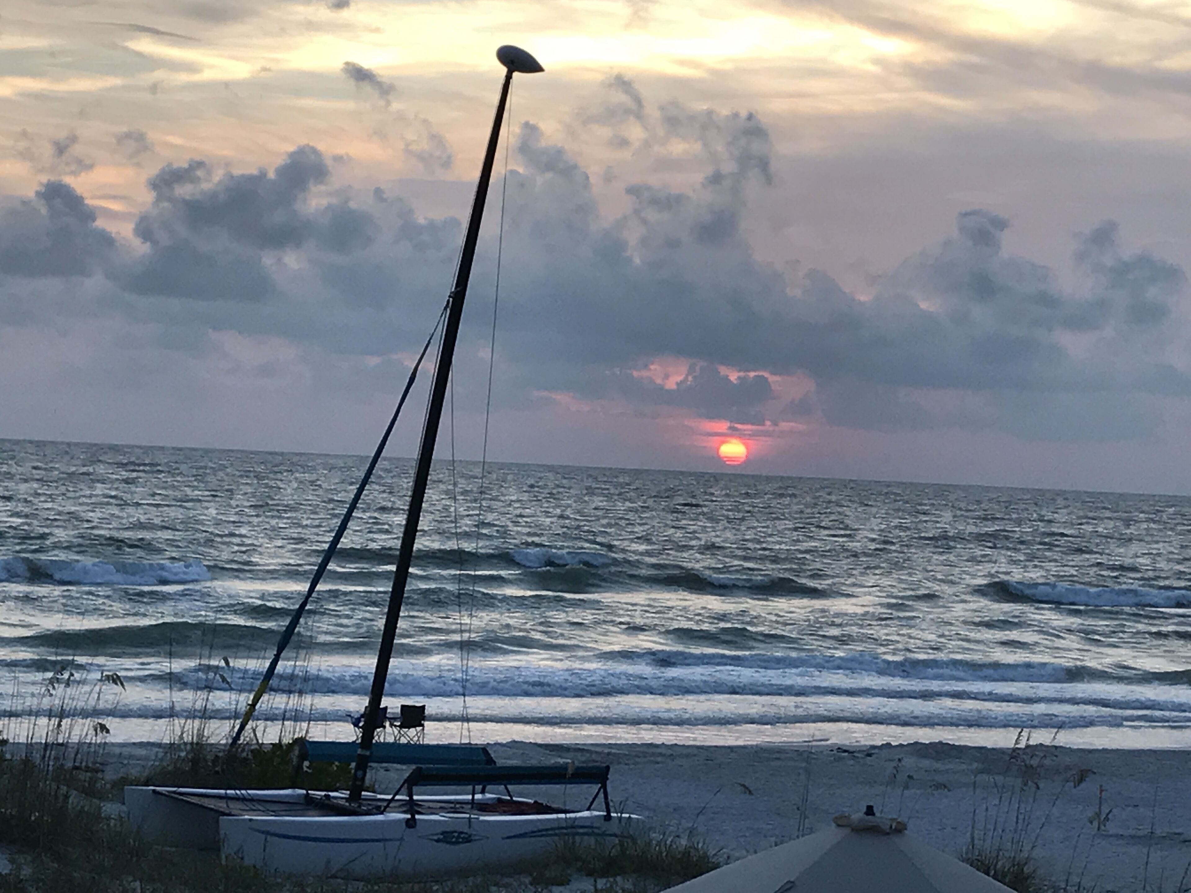 Um veleiro numa praia com o pôr do sol ao fundo.