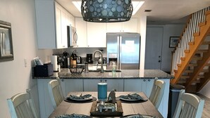 Comedor con mesa de madera, sillas blancas y una isla central con un jarrón azul.