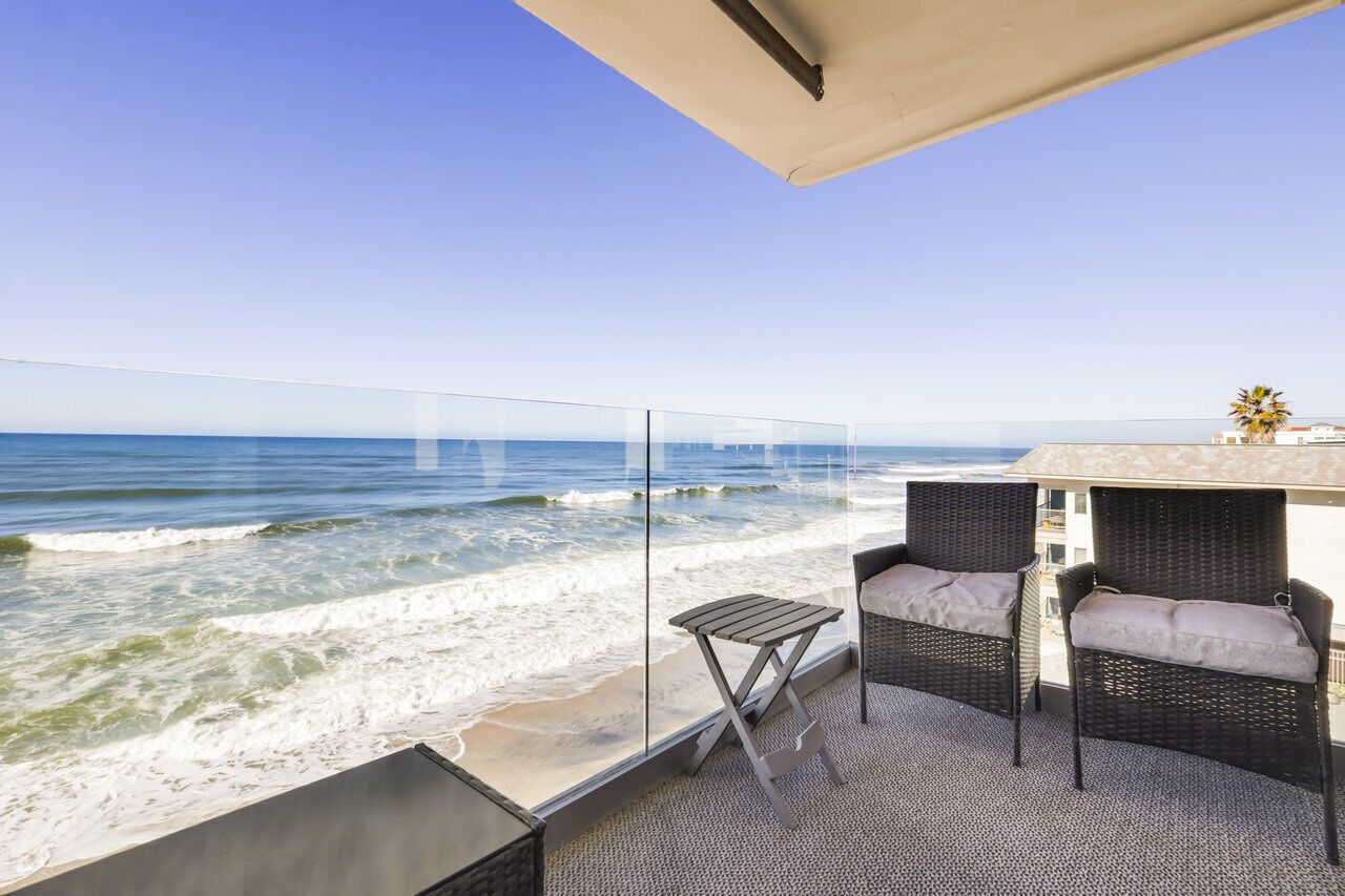 Een balkon met rieten meubilair en een glazen balustrade met uitzicht op de oceaan.