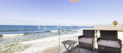Een balkon met rieten meubilair en een glazen balustrade met uitzicht op de oceaan.