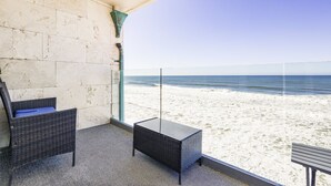 En balkon med fletmøbler, gelænder af glas og udsigt til stranden.