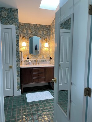 Une salle de bain avec un meuble-lavabo double, deux appliques murales, un miroir et un mur décoré d’un motif.