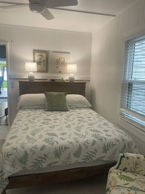 Quarto com uma cama, uma mesa de cabeceira com duas luminárias, um travesseiro verde e uma janela com persianas.