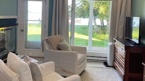 Una habitación con ventilador de techo, un ventanal con cortinas, televisión y chimenea.