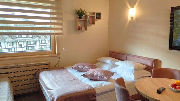 Habitación de hotel con cama, mesita de noche, silla y una pequeña mesa redonda con un bol de fruta.