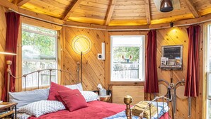 Une pièce de cabane en bois comprenant un lit, une table, une lampe et une fenêtre avec des rideaux.