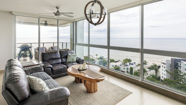 Uma sala de estar espaçosa com uma janela grande que oferece vista para o mar e edifícios.