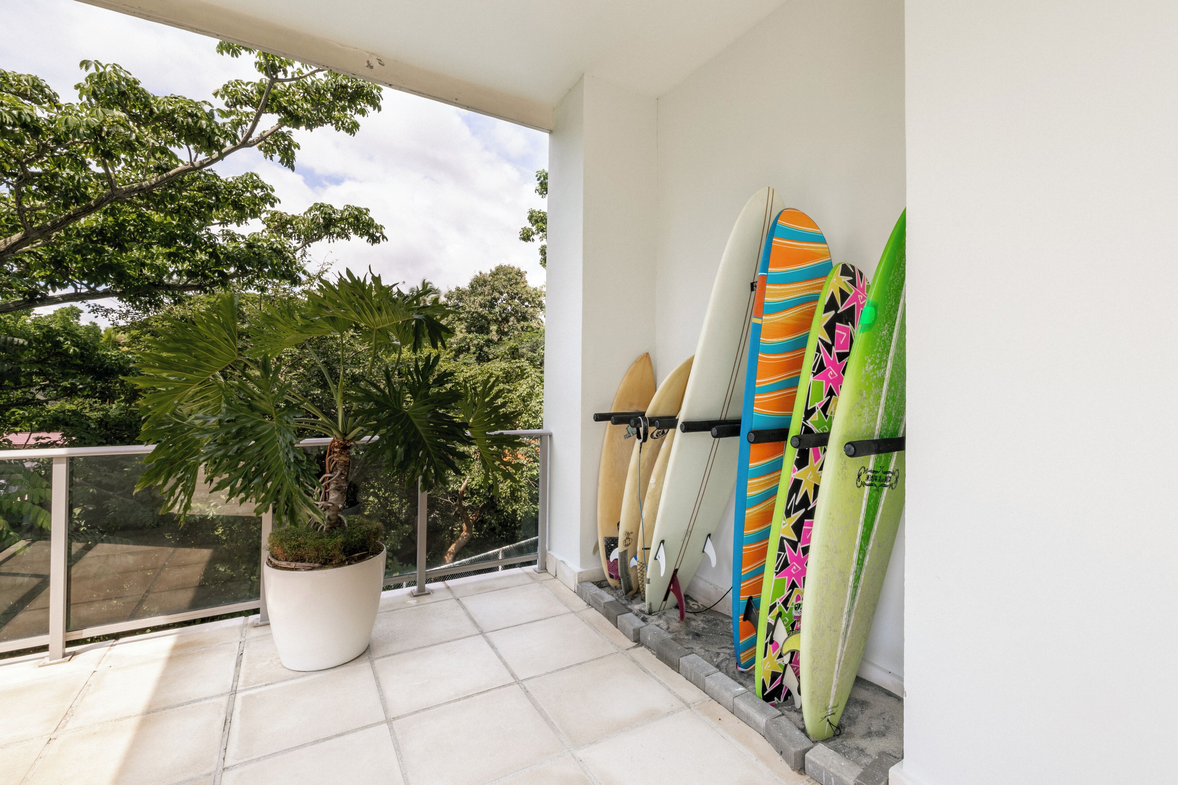 Un balcon avec un pot de fleurs et plusieurs planches de surf appuyées contre le mur.