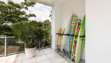 Un balcon avec un pot de fleurs et plusieurs planches de surf appuyées contre le mur.