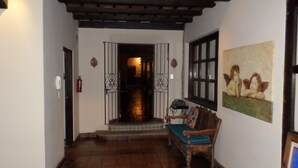 A hallway with a wooden ceiling, a bench with a cushion, a painting of cherubs, and a door with a metal gate. - La Casa de Don Pedro, Beautiful house in Antigua Guatemala (Antigua Guatemala)