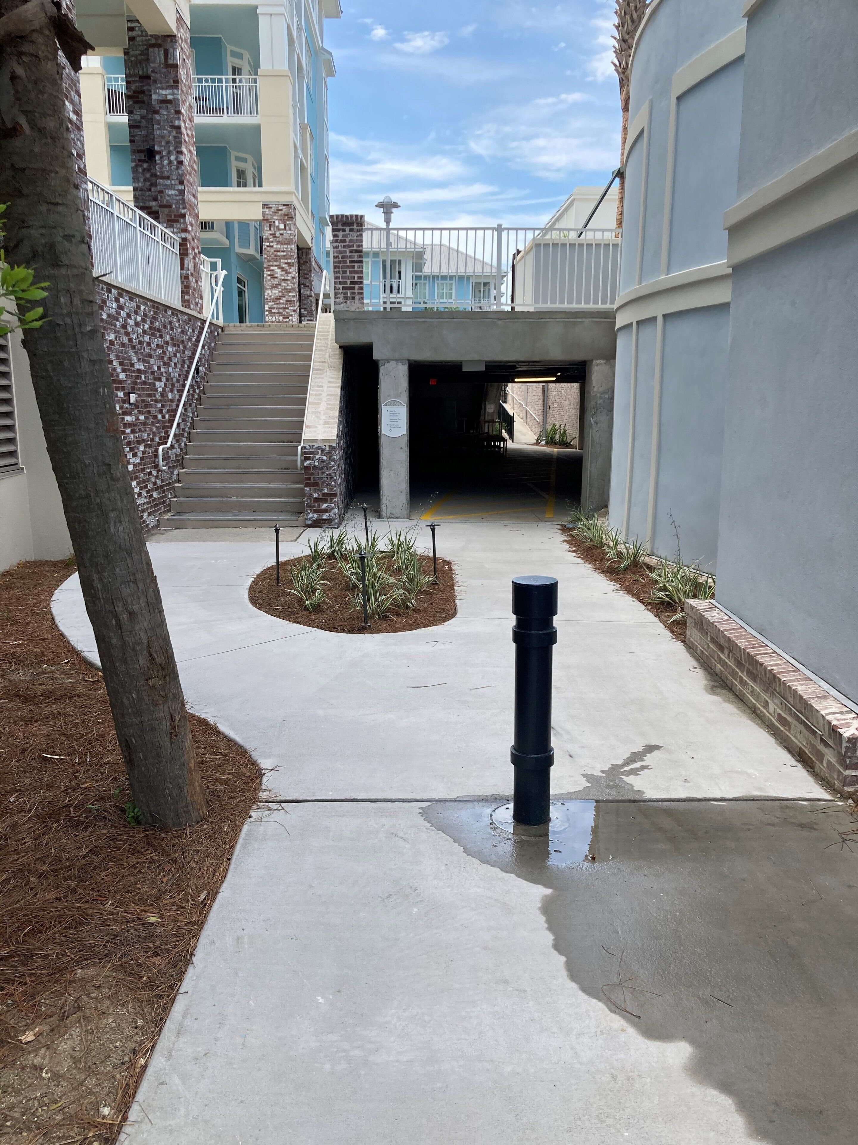 L’entrée d’un immeuble est marquée par un escalier en béton menant à un espace abrité, entouré de murs en briques et d’un petit jardin.