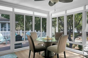 A sunroom with a glass table and four chairs, large windows, and a ceiling fan.