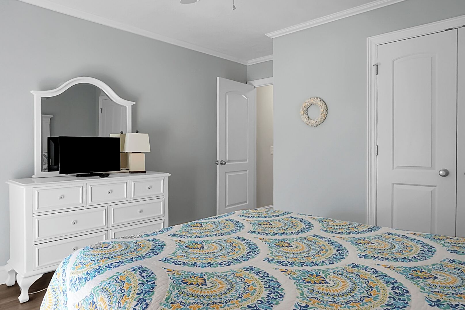 A bedroom with a bed, dresser, television, and two doors.