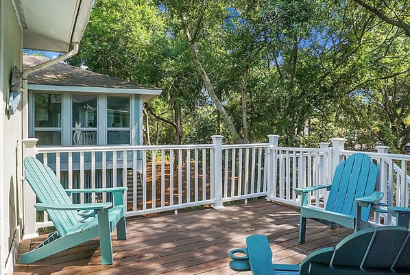 A wooden deck with a white railing, surrounded by trees.