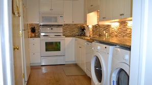 Una cocina compacta con armarios blancos, microondas, horno, lavaplatos y lavadora.