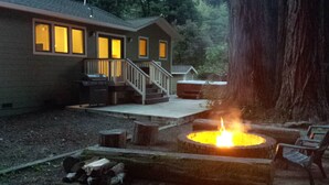A cabin with a fire pit, wooden deck, and a large tree in the background. - A Family Retreat Among the Redwoods. (Cazadero)