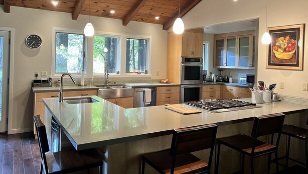 A modern kitchen with a large island, wooden ceiling beams, and large windows. - A Family Retreat Among the Redwoods. (Cazadero)