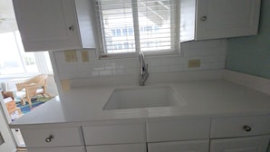Una cocina con armarios blancos, un lavamanos y una ventana con persianas.