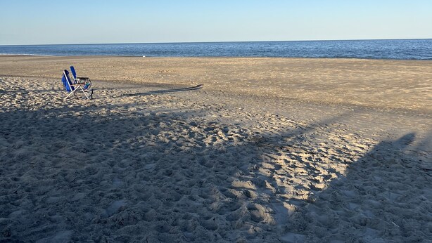 Una playa con una sola silla azul y un cielo azul despejado.