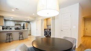 A modern kitchen with grey cabinets, a central island with stools, a dining area with a round table and grey chairs, and a laundry area with a washing machine and dryer.
