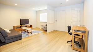 A modern living room with a sofa, TV, wooden desk, and chairs.