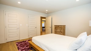 A bedroom with a bed, a wooden dresser, and two white doors.