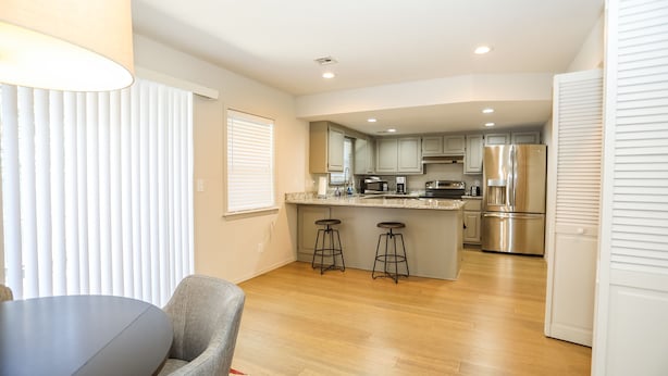 A modern kitchen with wooden flooring, a central island with stools, stainless steel appliances, and a dining area with a table and chairs.