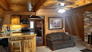 Interior acogedor de una cabaña con techo de madera, comedor, chimenea y sala de estar con sofá a cuadros.
