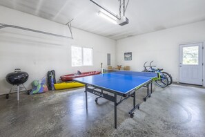 A ping pong table in a room with a concrete floor, a door, and a bicycle. - Waterfront | Hot Tub | Kayaks | Crab Traps | 3~Kings (Lincoln City)