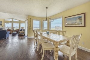 Un espace repas avec une table et des chaises en bois, de grandes fenêtres et une vue sur l’extérieur.