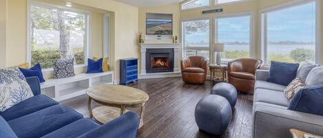 A spacious living room with a fireplace, large windows, and a view of the outdoors.